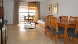 A dining area with a table and chairs, a sofa, a glass coffee table, and a window with curtains. - Family apartment with pool - 6 guests (Gandía)