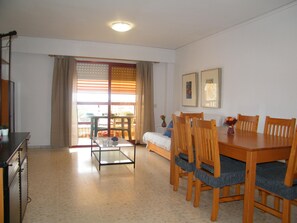 A dining area with a table and chairs, a sofa, a glass coffee table, and a window with curtains. - Family apartment with pool - 6 guests (Gandía)