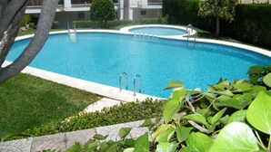 A swimming pool surrounded by greenery, with a building in the background. - Family apartment with pool - 6 guests (Gandía)