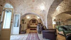 Una habitación amplia con paredes de piedra y techo abovedado, que incluye un sofá, una silla y un jarrón grande.