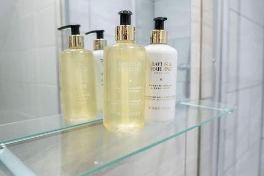 A bathroom with a glass shelf holding bottles of Bayti is & Harimaging products.