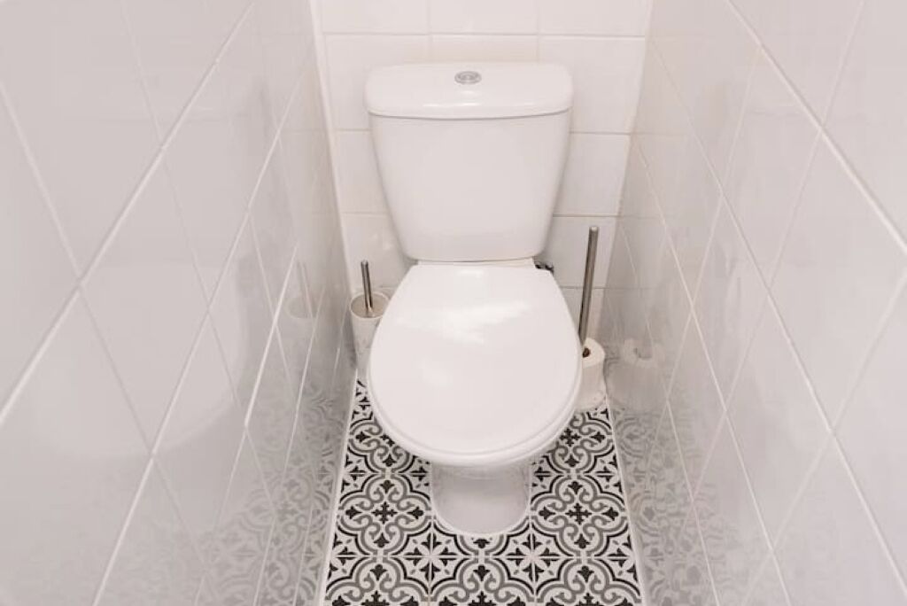 Een badkamer met een wit toilet, betegelde wanden en een vloer met een patroon.