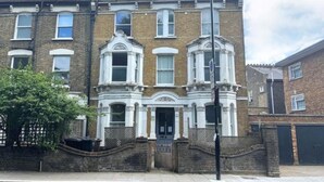 A two-story brick building with a central bay window, a gated entrance, and a street lamp. - Charming Camden Town Retreat with Garden – Walk to Market & Transport (London)