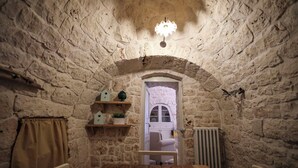 Una habitación pequeña con paredes de piedra, una mesa de madera, un radiador y una silla blanca.