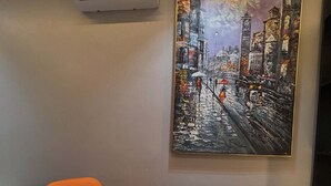 A room with a modern orange chair, a small round table, and a large cityscape painting on the wall. - Deroj Western Hotel (Benin City)