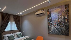 A modern bedroom with a bed, an air conditioner, a painting, a chair, and a small table. - Deroj Western Hotel (Benin City)