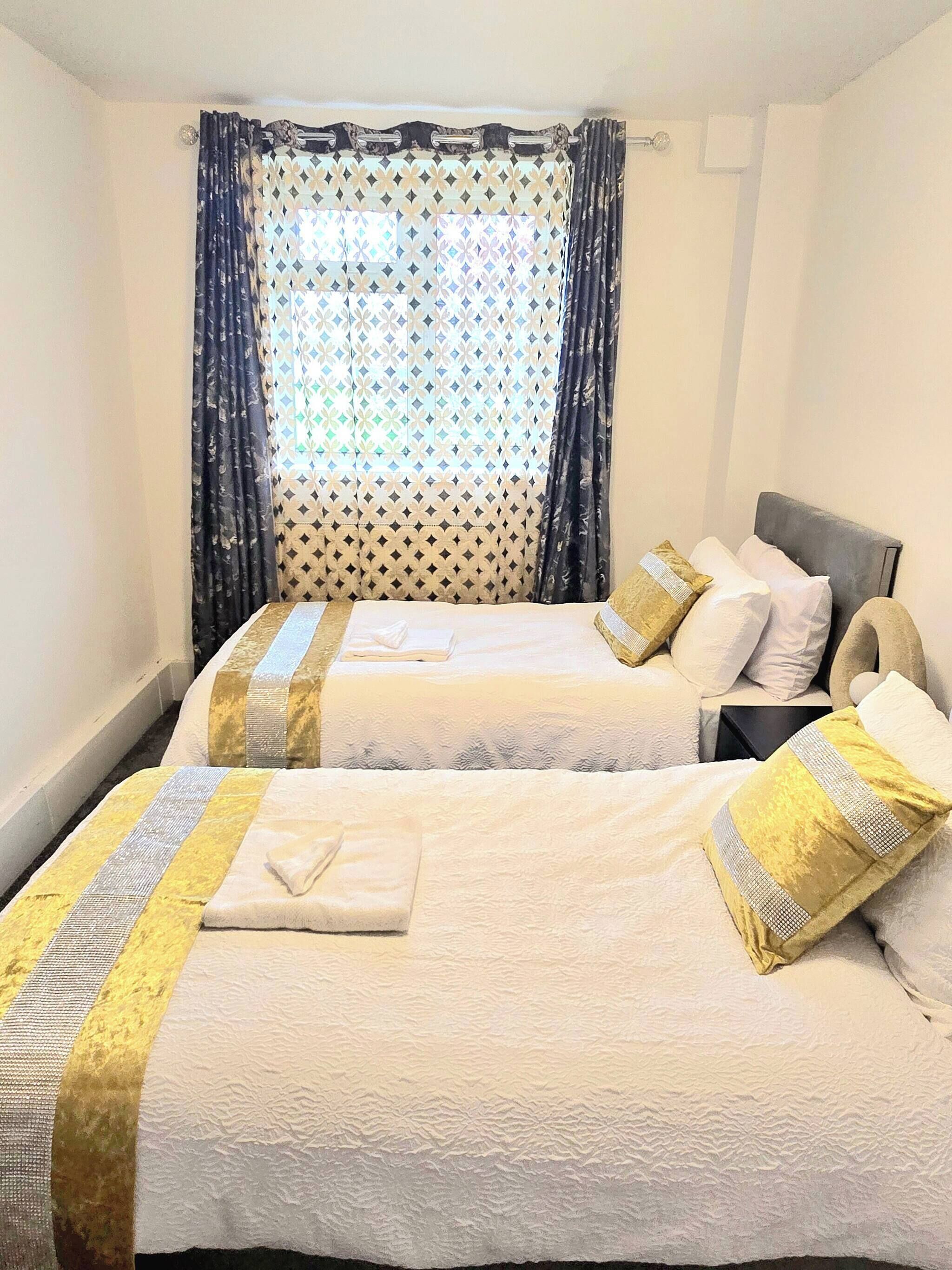Quarto de hotel com duas camas, cada uma com cabeceira, almofadas e cobertor.