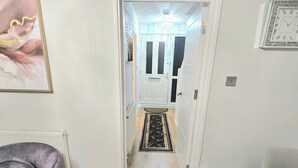 A modern living room with a leather sofa, a dining table set with plates and cutlery, and a hallway leading to a door with a chandelier. - Gem Place - A Home Away From Home (Hornchurch)