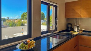 Une cuisine moderne avec une grande fenêtre, un saladier rempli de fruits sur le plan de travail et une machine à café.