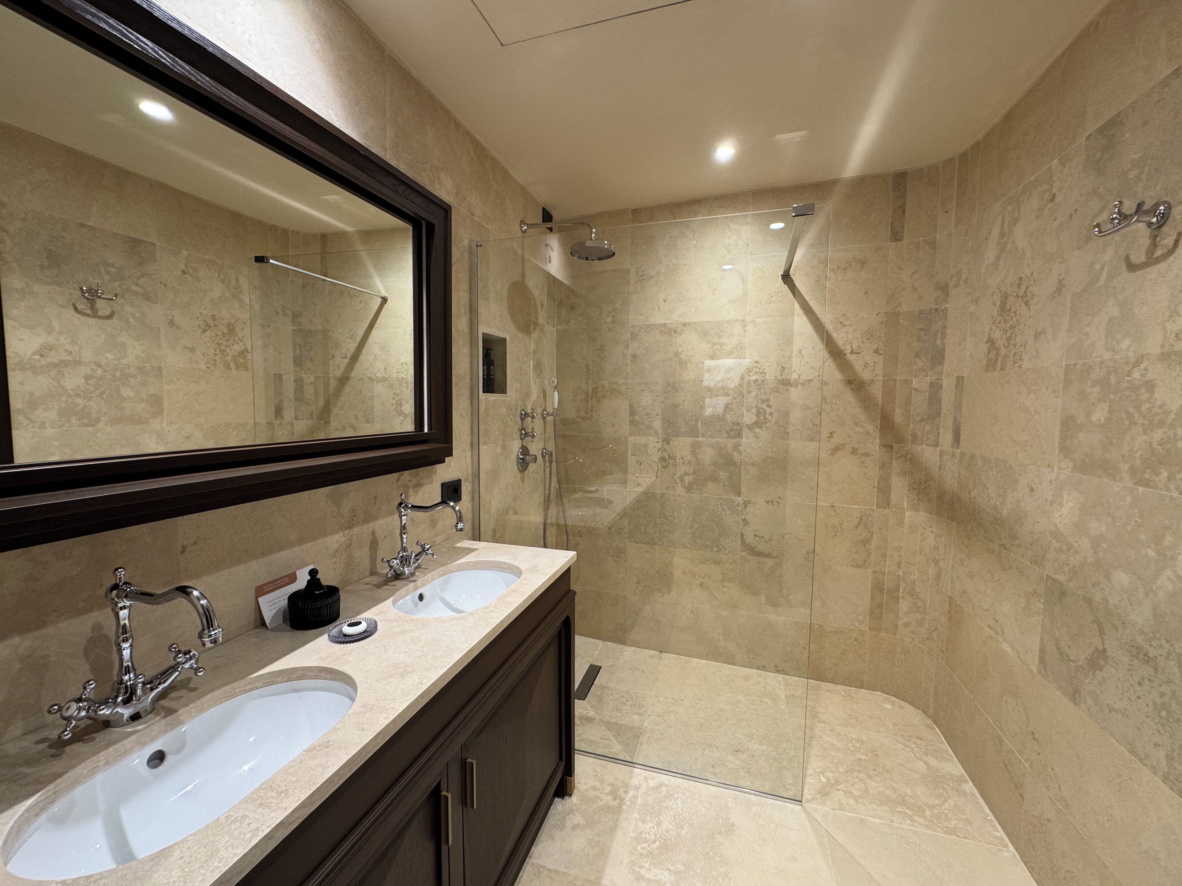 A modern bathroom with two sinks, a large mirror, and a glass-enclosed shower area.