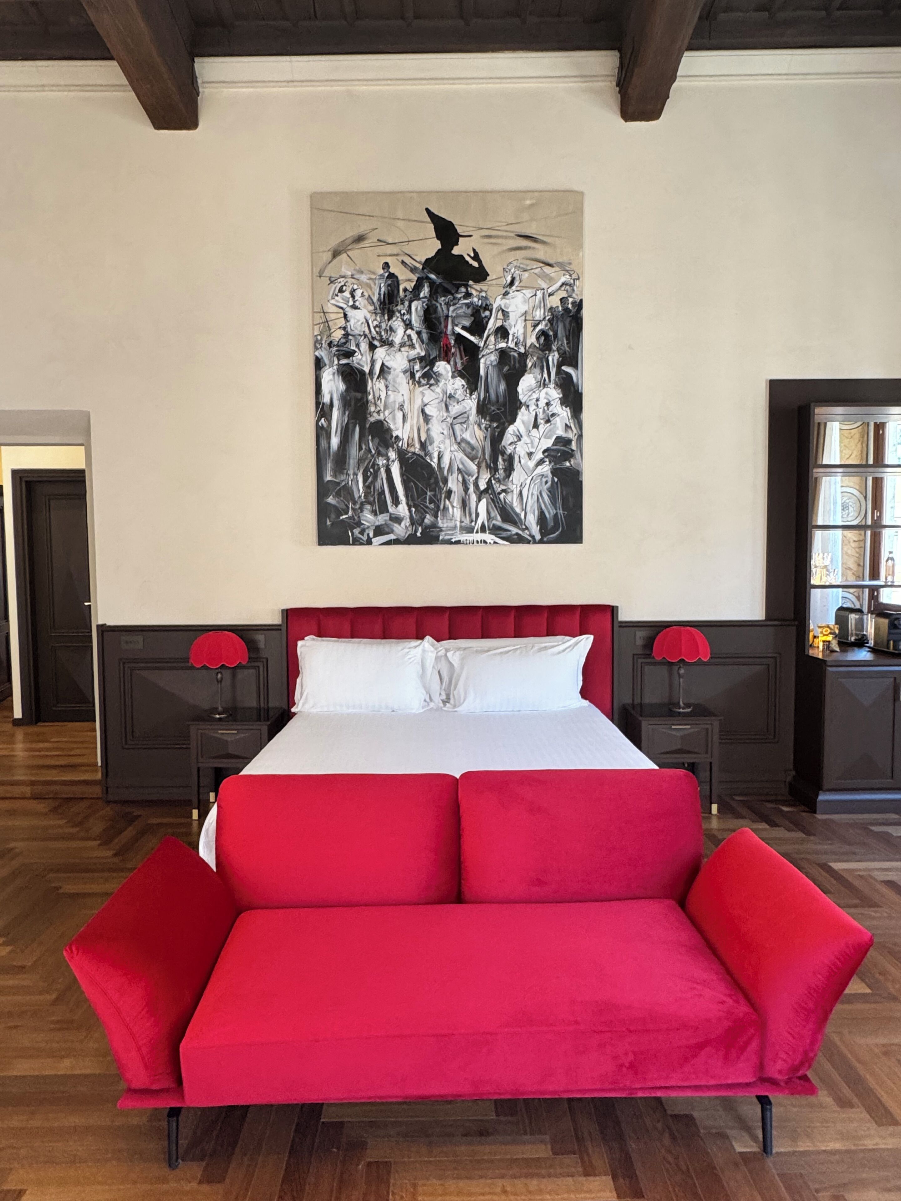 Un dormitorio con una cama grande, dos mesitas de noche con lámparas, un sofá rojo y un cuadro blanco y negro en la pared.