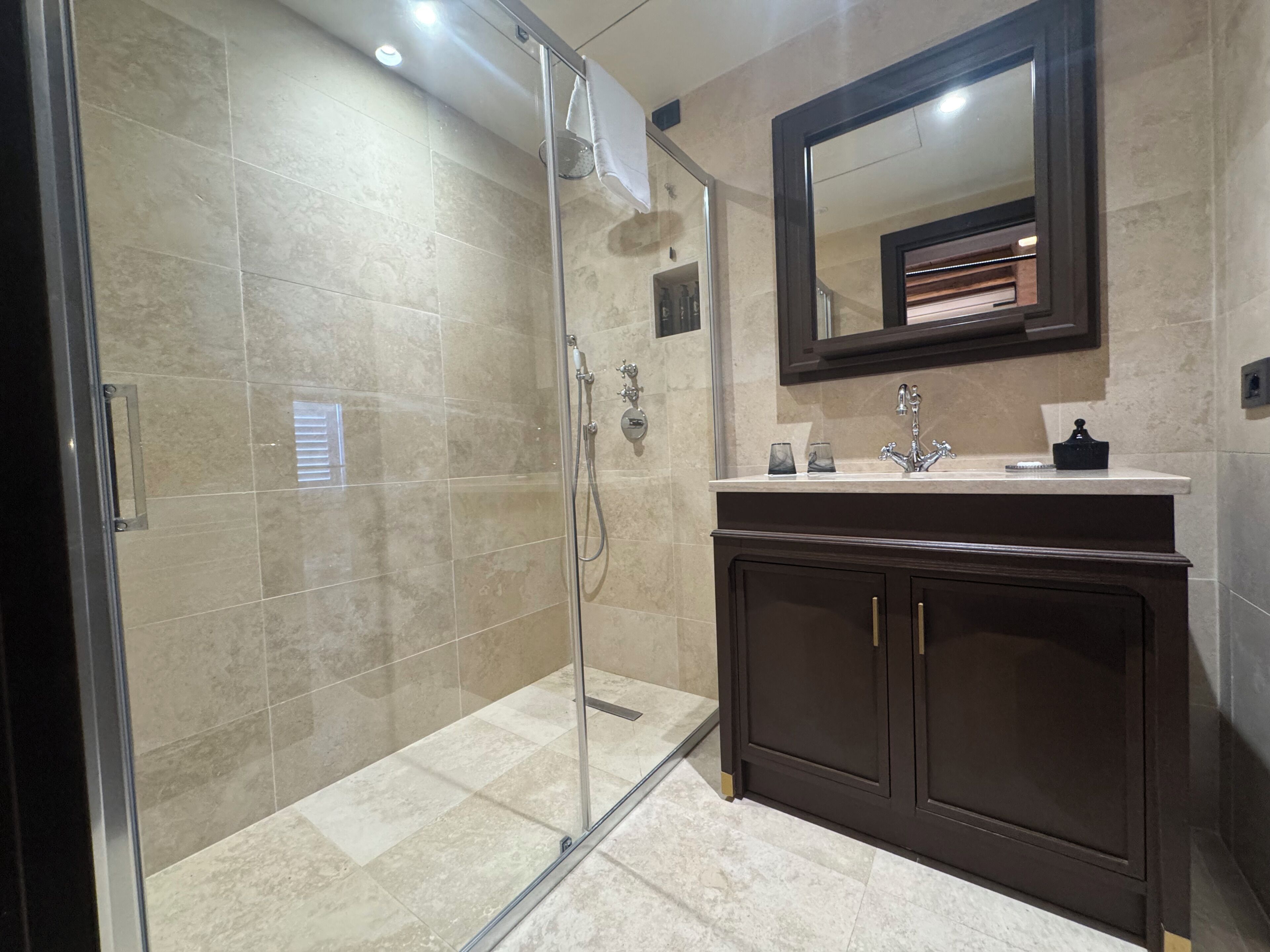 Un baño con ducha de mampara de vidrio, tocador de madera oscura y espejo sobre el lavabo.