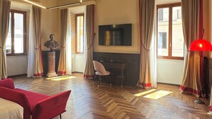 Una habitación con piso de parqué, un sofá rojo, un escritorio con una silla, un televisor y una estatua.