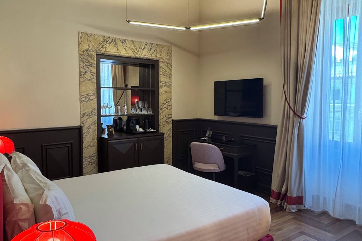 A hotel room with a bed, a desk, a television, a mirror, and a window with curtains.