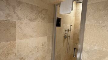 A glass-enclosed shower with beige tiles, a towel hanging on the door, and a showerhead.