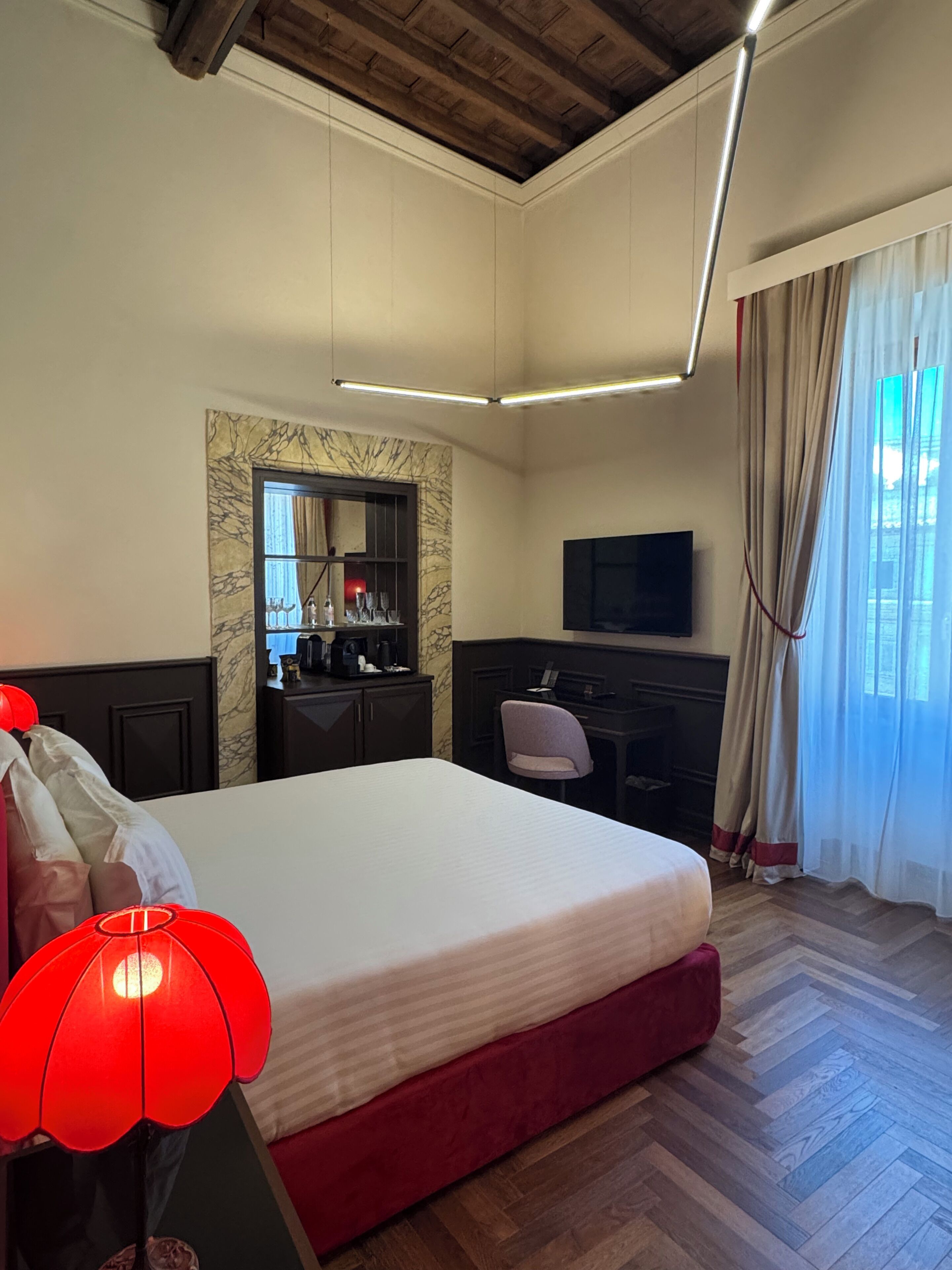 A hotel room with a bed, a desk, a television, a mirror, and a window with curtains.