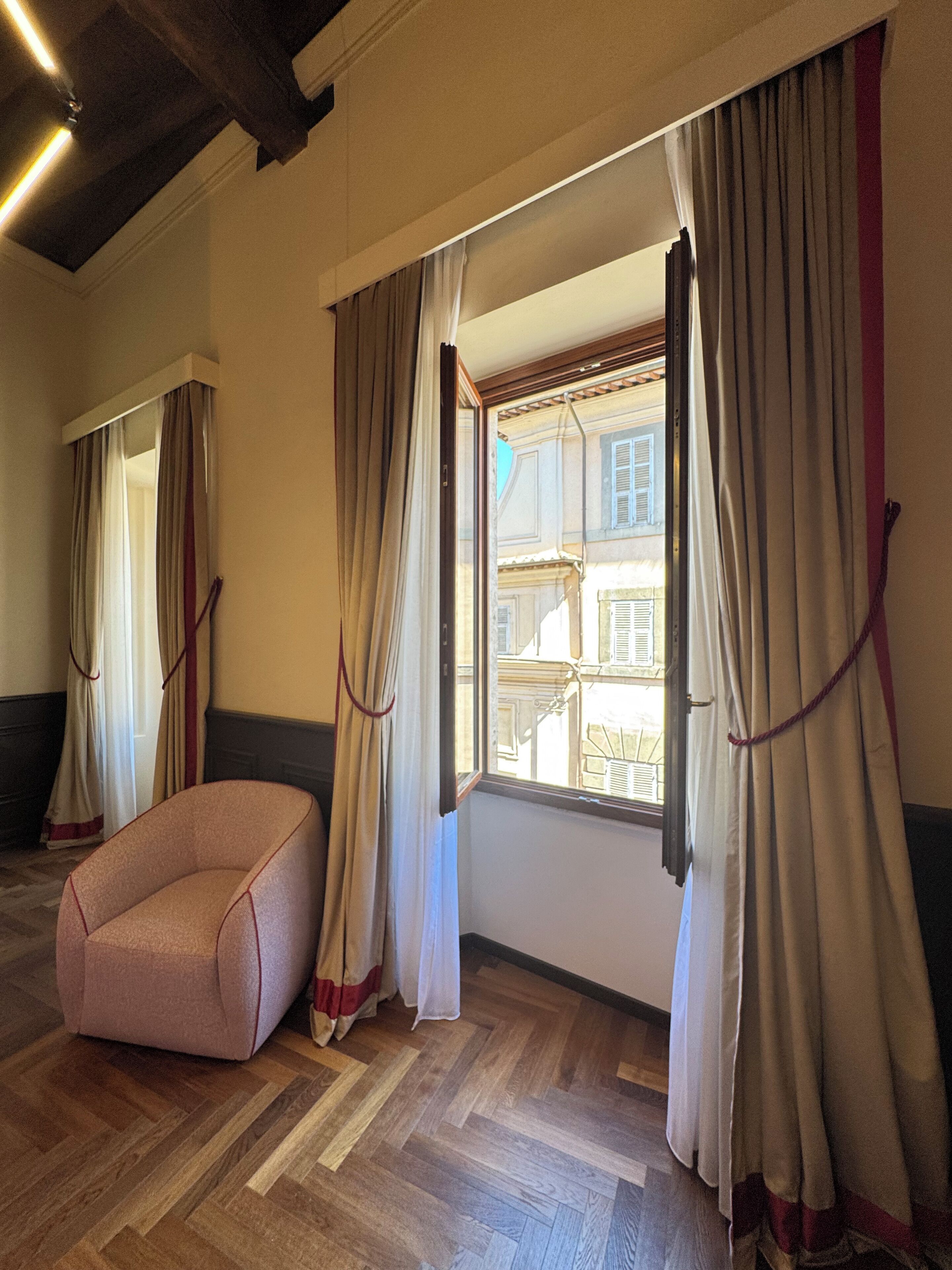 A room with a herringbone floor, a pink bean bag chair, and a window with curtains.