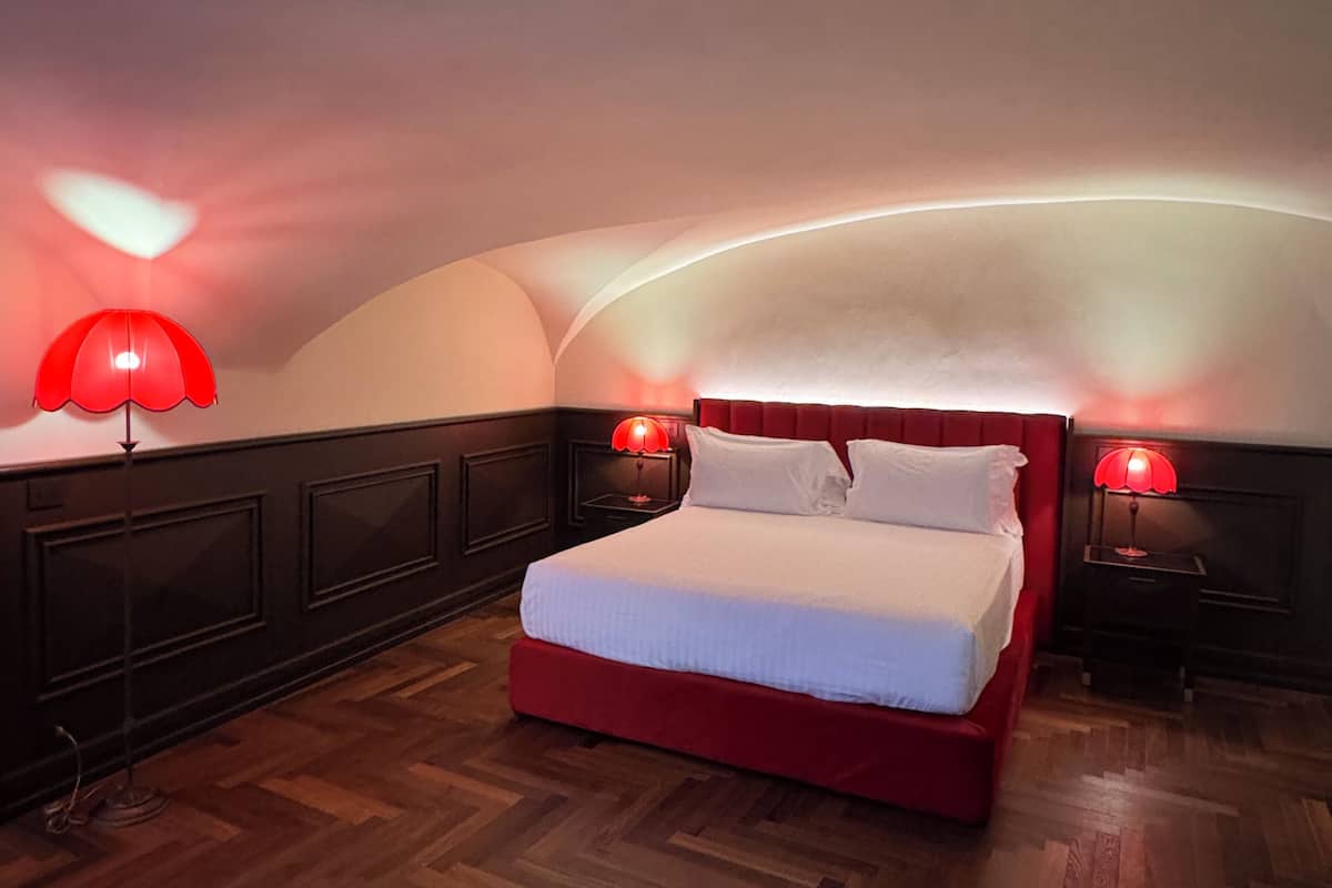 A bedroom with a red bed, two bedside lamps, a wooden herringbone floor, and a curved ceiling.