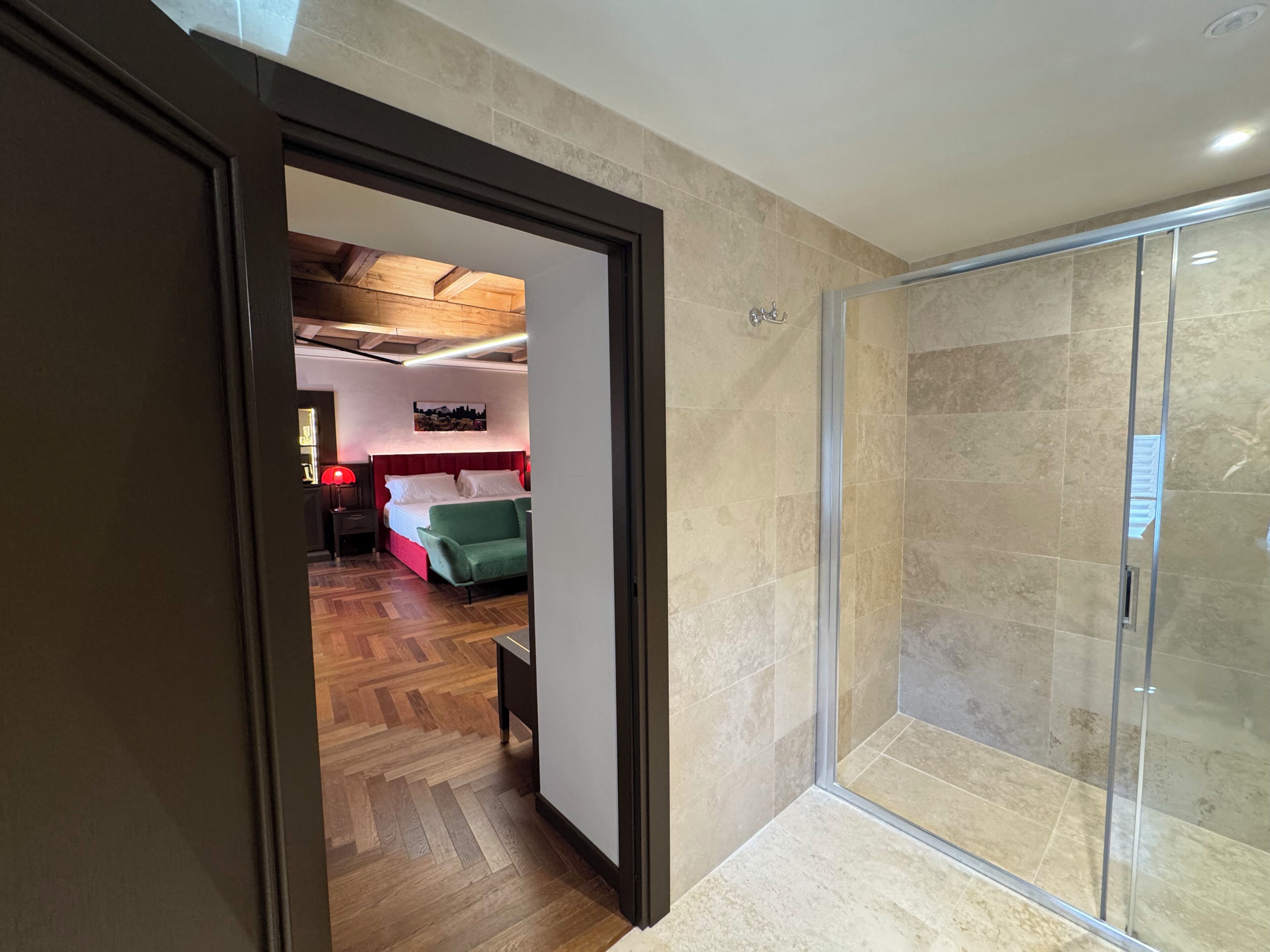 A hotel room with a wooden floor, a glass shower, and a bed with green bedding.