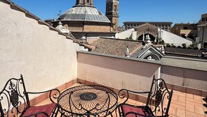 Una terraza con mesa y sillas, vista a una iglesia con cúpula y campanario, y techo de tejas.