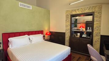 Een kamer met een bed, een bureau, een stoel, een spiegel en een kitchenette.