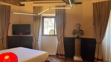 A room with a bed, a flat-screen TV, a bust sculpture, and a window with curtains.