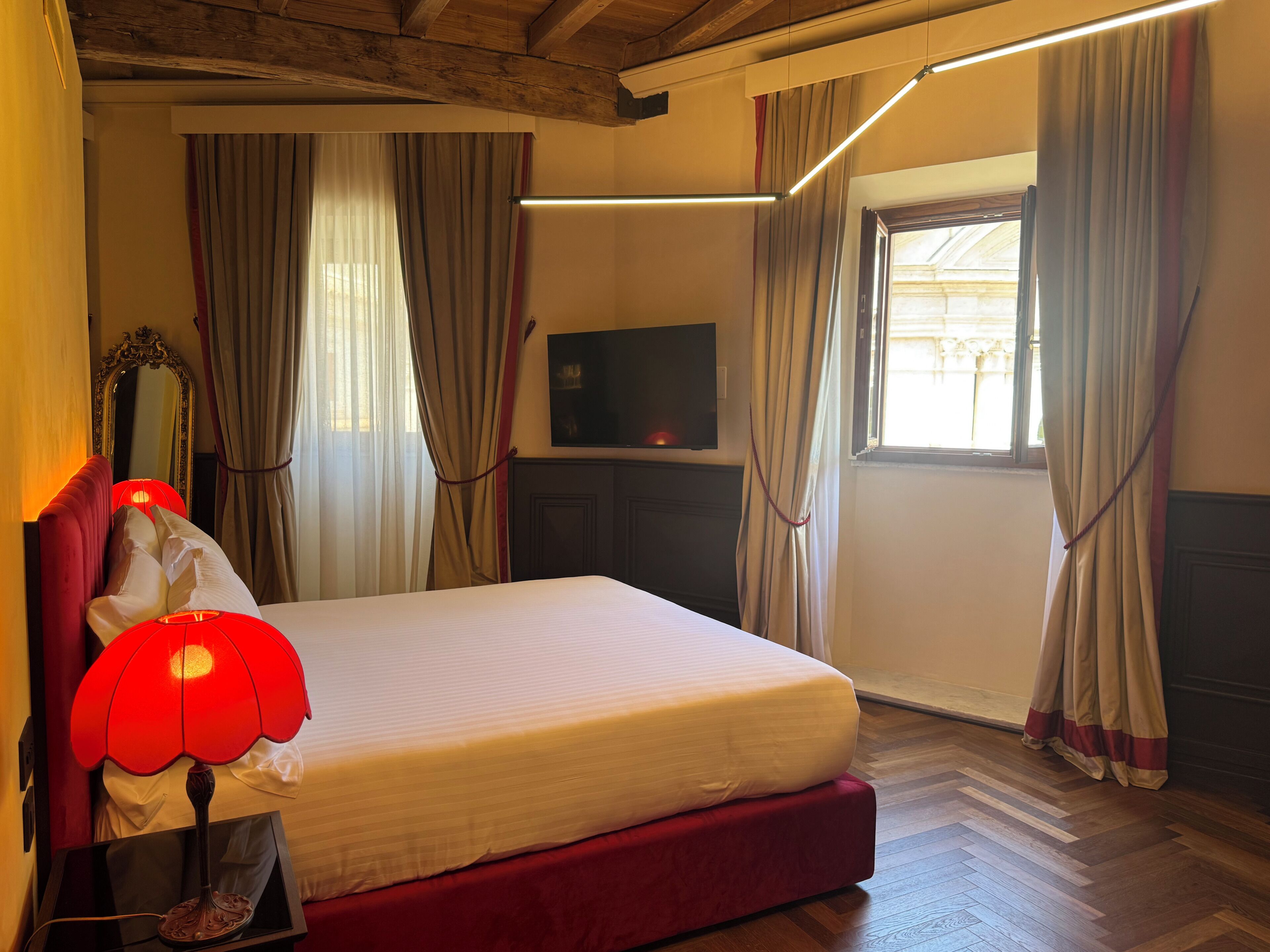 Una habitación de hotel con cama, televisión, una lámpara roja y cortinas.