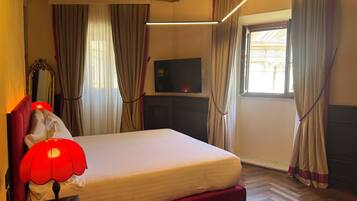 Una habitación de hotel con cama, televisión, una lámpara roja y cortinas.