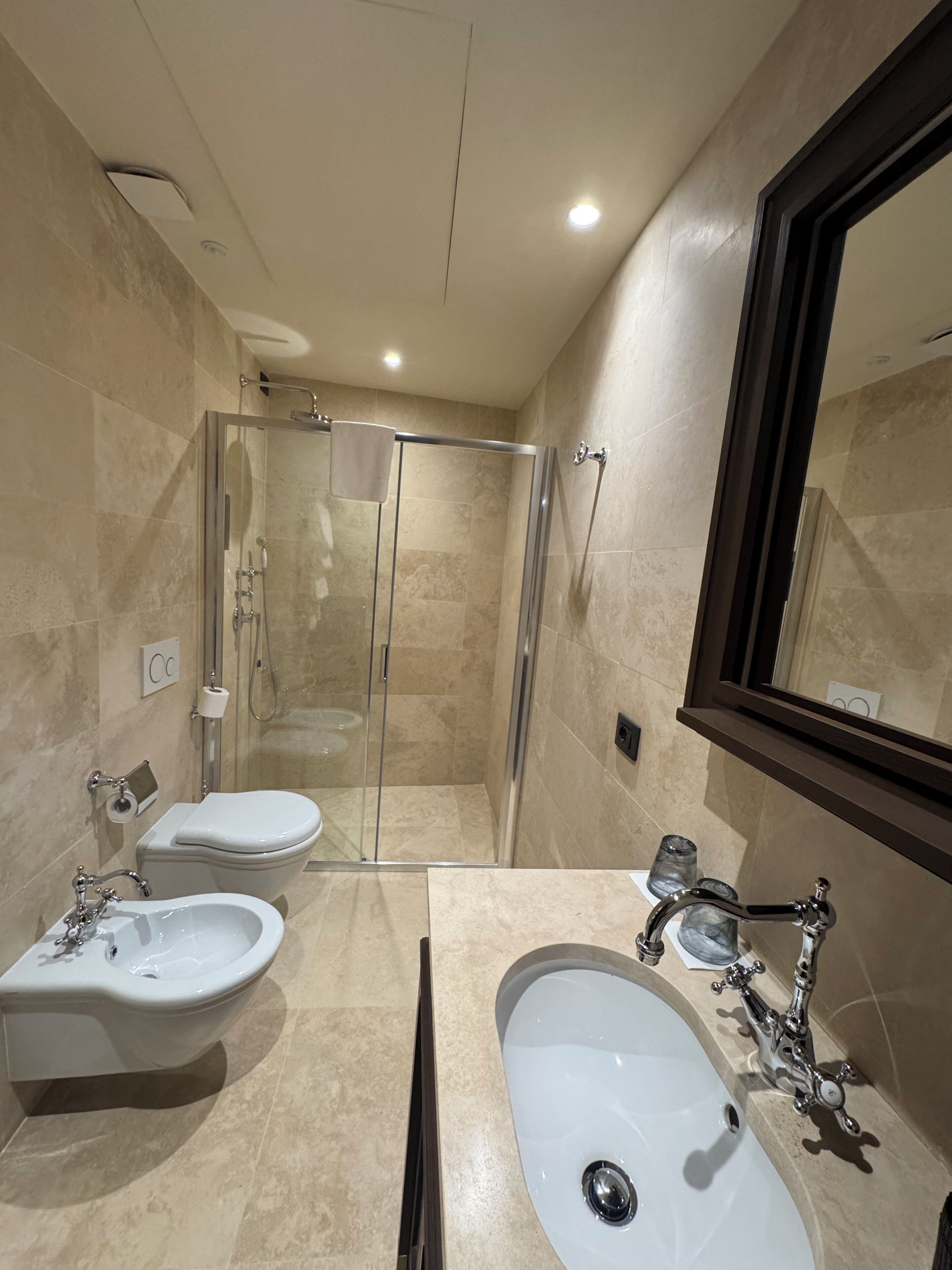 A modern bathroom with a glass-enclosed shower, two sinks, a toilet, and a large mirror.