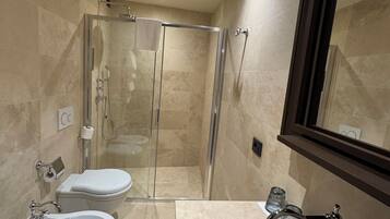 A modern bathroom with a glass-enclosed shower, two sinks, a toilet, and a large mirror.