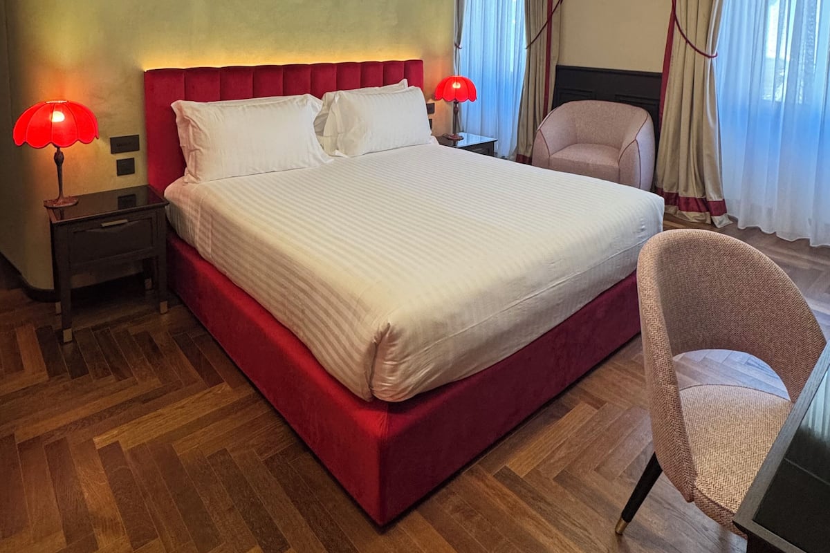 A hotel room with a large bed, two bedside lamps, a chair, and a desk.