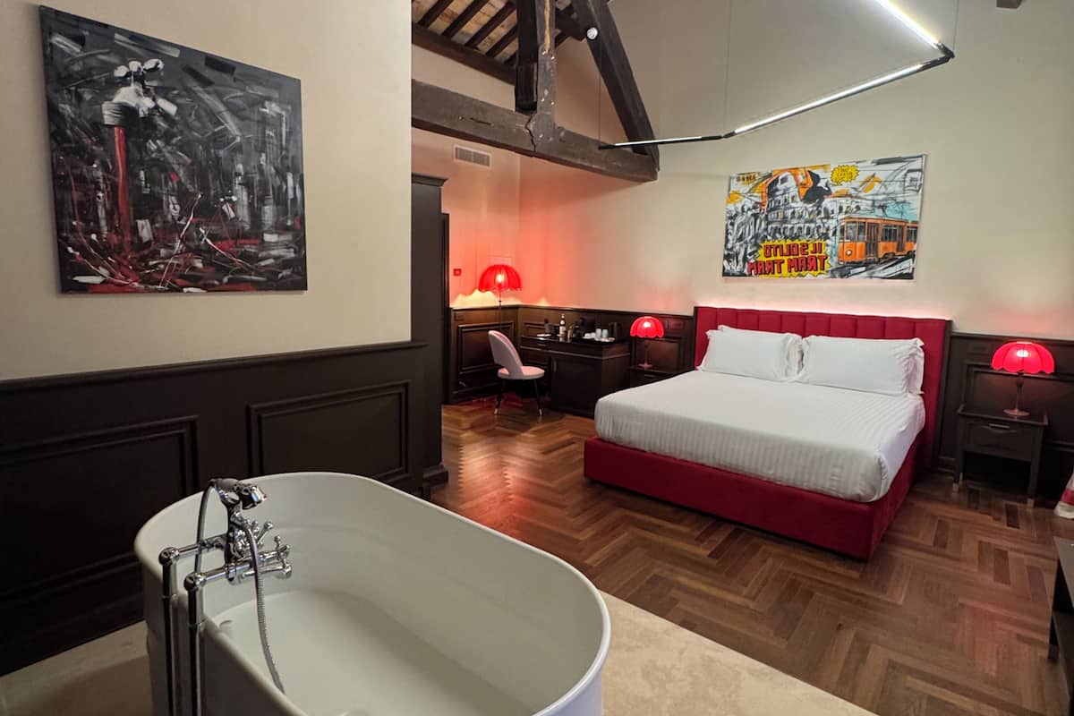 A bedroom with a large bathtub, a bed with red bedding, and a wooden ceiling.