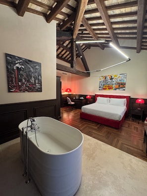 Un dormitorio con una bañera grande, una cama con ropa de cama roja y un techo de madera.