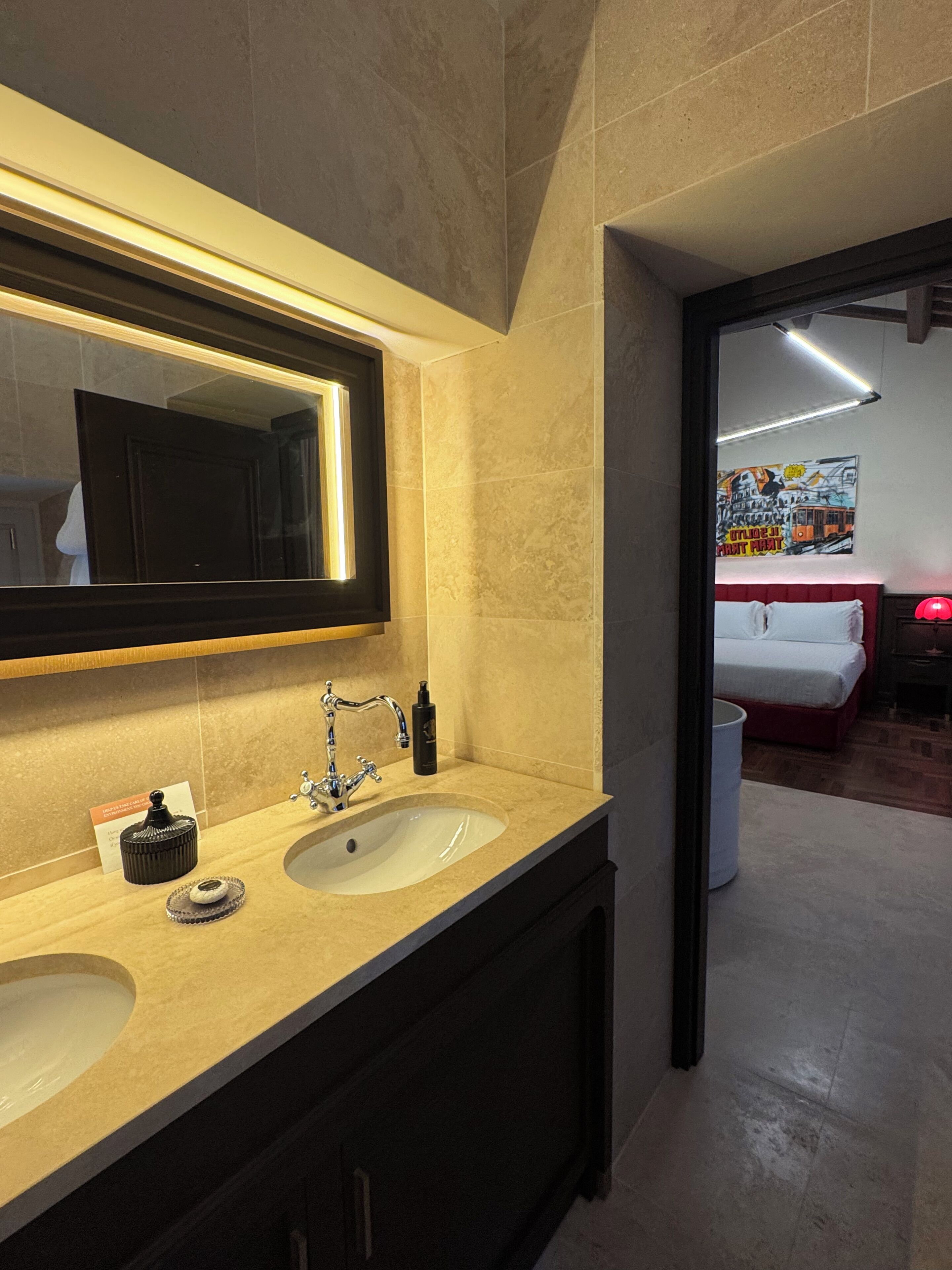 A modern bathroom with a double sink, a large mirror, and a red lamp.