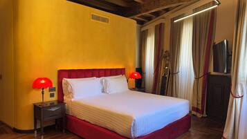 A hotel room with a large bed, wooden flooring, a red upholstered headboard, two bedside lamps, and a mirror.