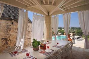 A dining area with a table set for two, a view of a pool, and a stone wall. - Wonderful private villa with A/C, private pool, WIFI, veranda, panoramic view, close to Alberobello (Locorotondo)