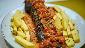 Ein Teller mit gegrilltem Fisch, gewürfelten Kartoffeln und Tomatensauce.