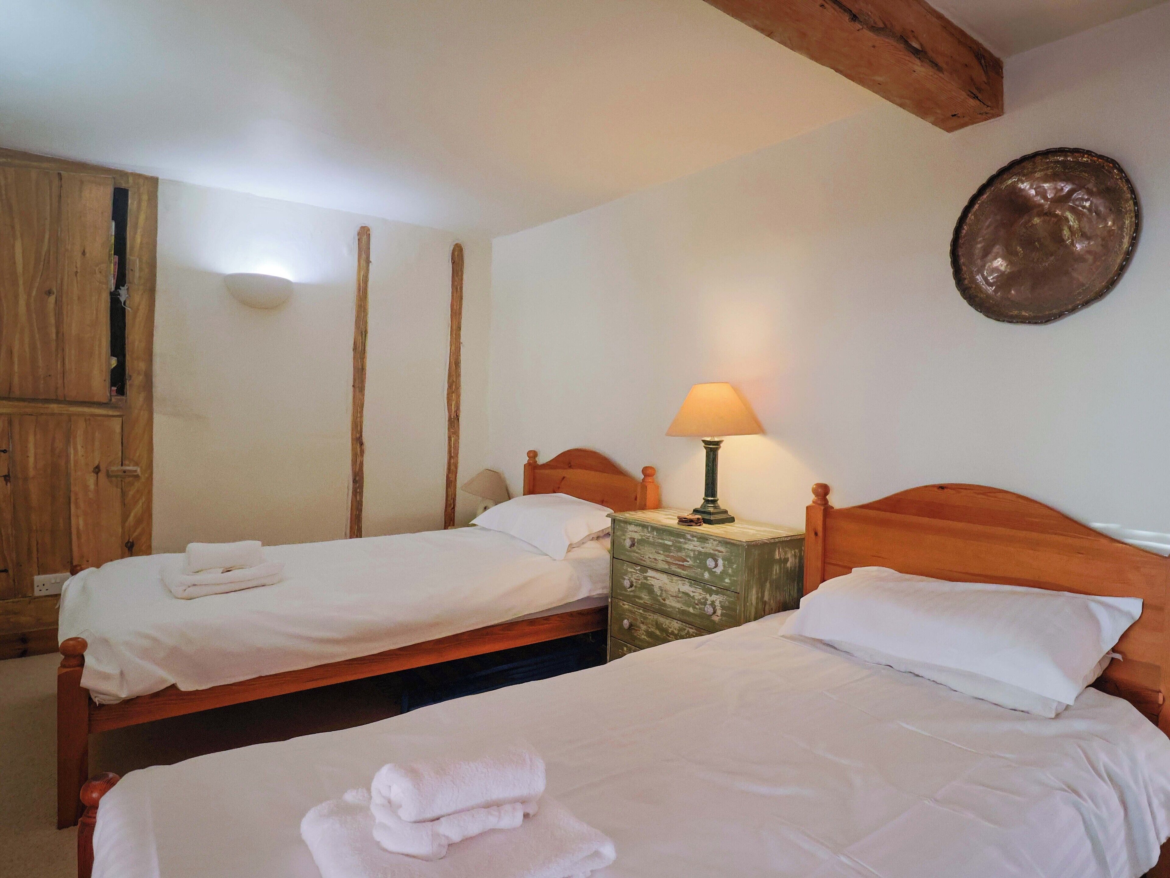 A room with two wooden beds, a wooden wardrobe, and a wall-mounted lamp.