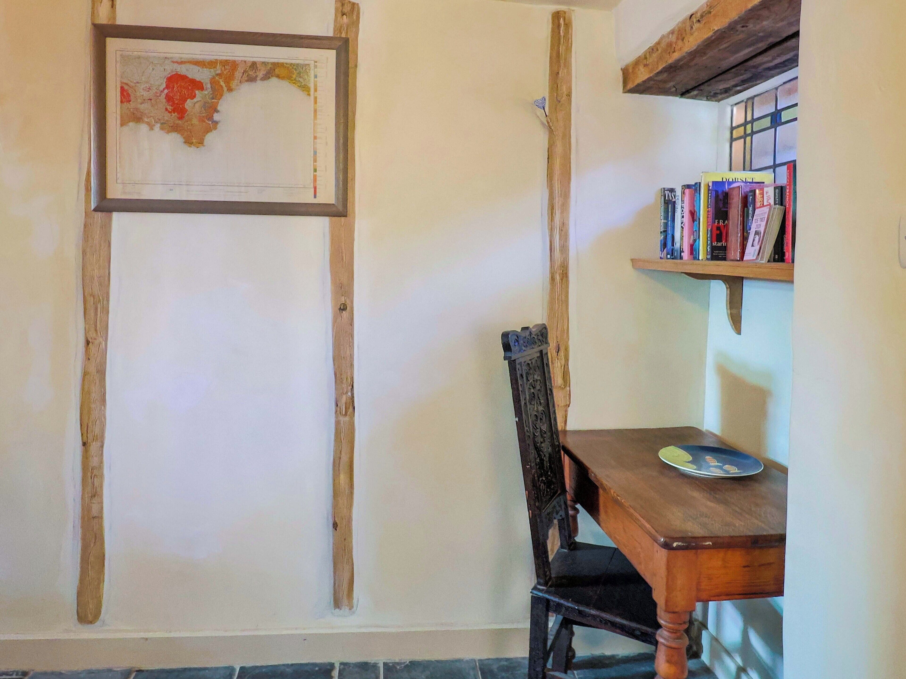Ein Zimmer mit einem Holztisch, einem Stuhl, einem Bücherregal und einer gerahmten Karte an der Wand.