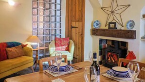 Uma sala de estar acolhedora com uma mesa de jantar de madeira posta para dois, lareira e uma decoração em forma de estrela na parede.