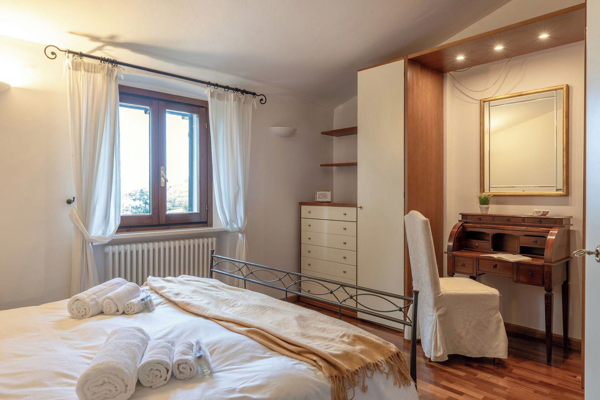 Ein Schlafzimmer mit einem Bett, einem Schminktisch, einem Frisiertisch und einem Fenster mit Vorhängen.