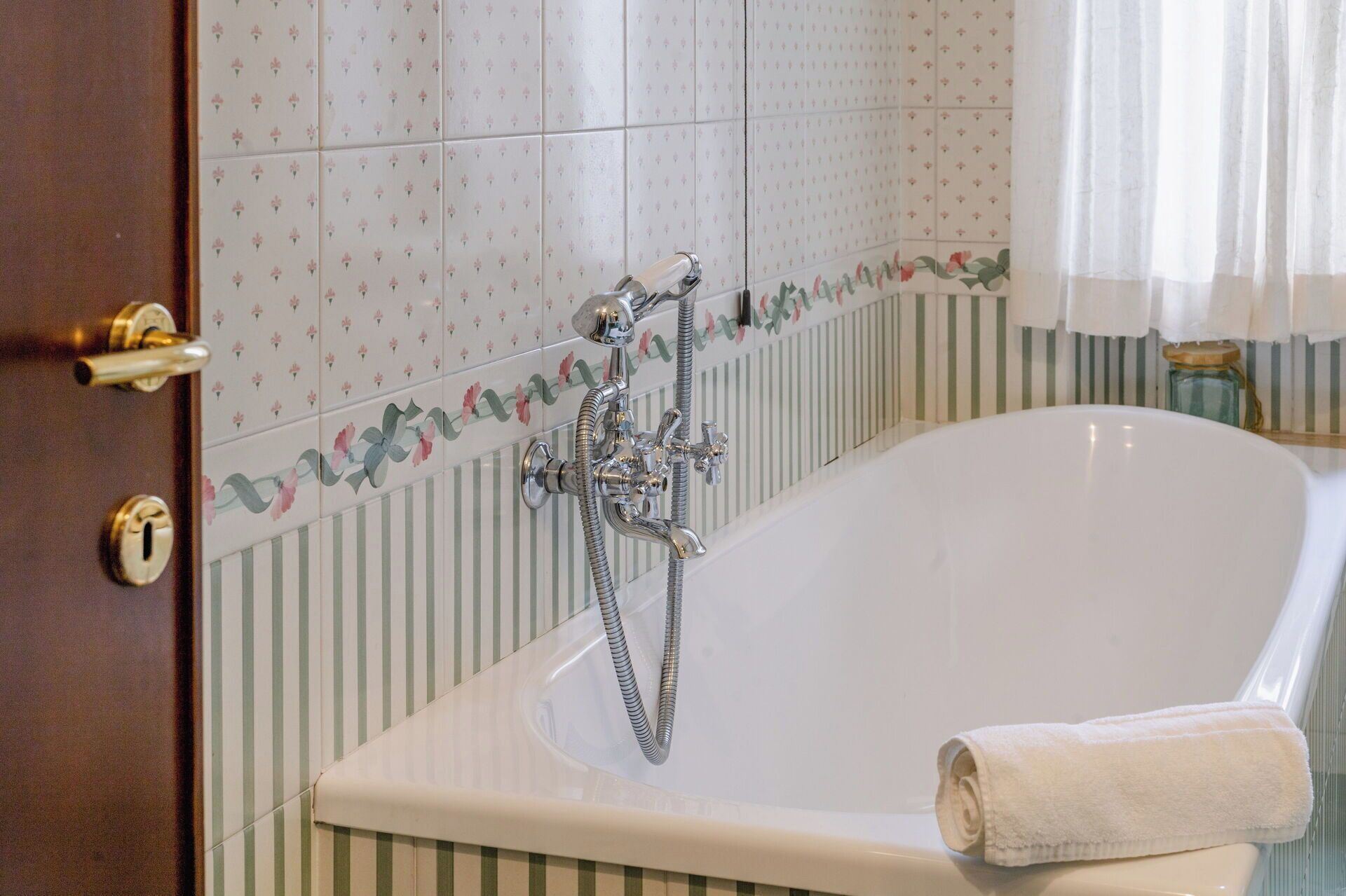 A bathroom with a white bathtub, a shower with a chrome faucet, and a striped wall design.