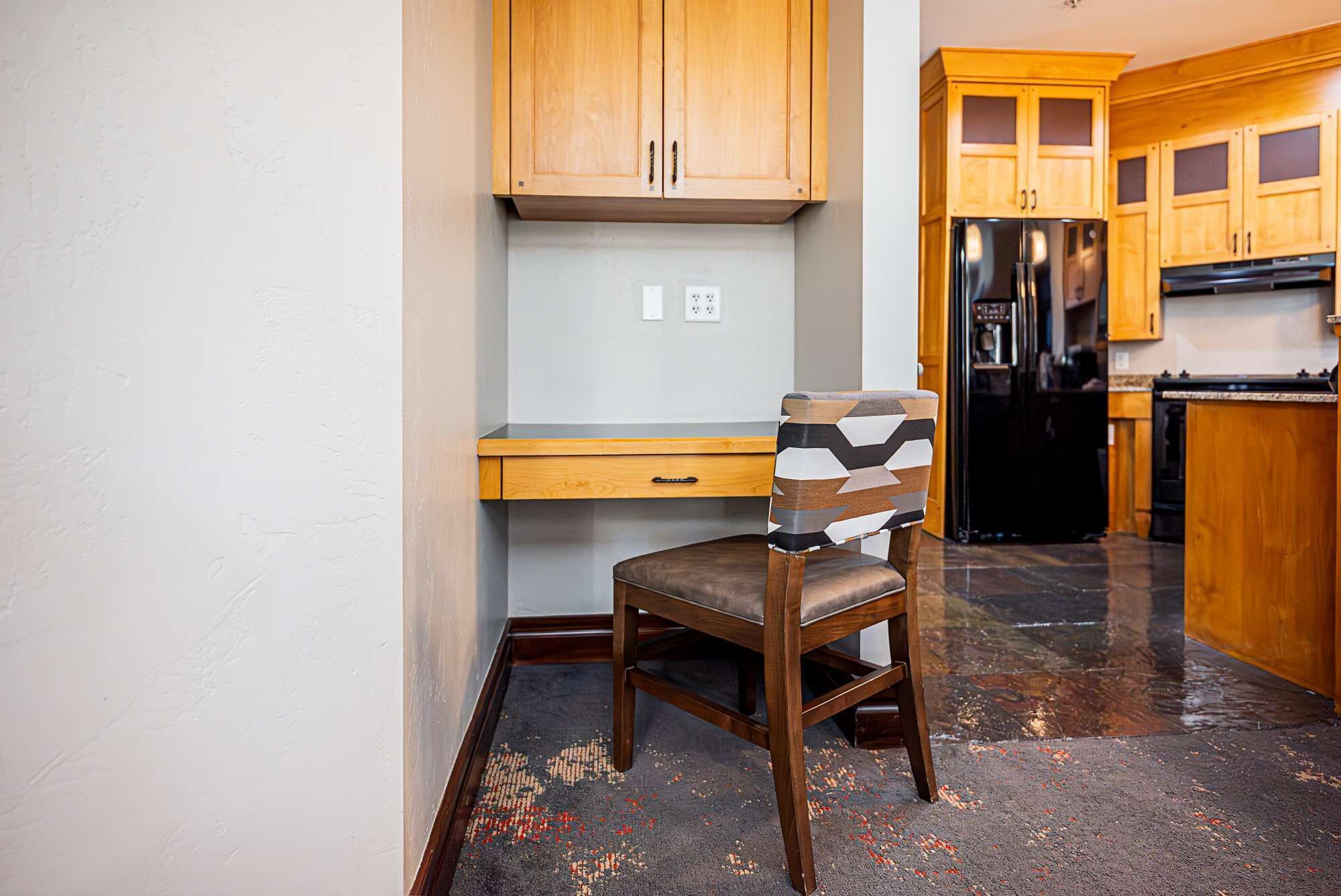 A kitchen with wooden cabinets, a black refrigerator, and a chair with a geometric-patterned backrest.