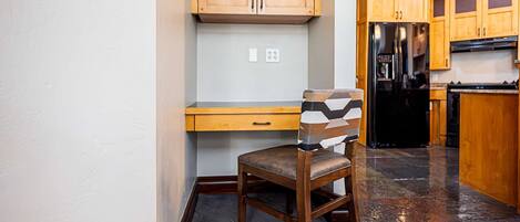 A kitchen with wooden cabinets, a black refrigerator, and a chair with a geometric-patterned backrest.