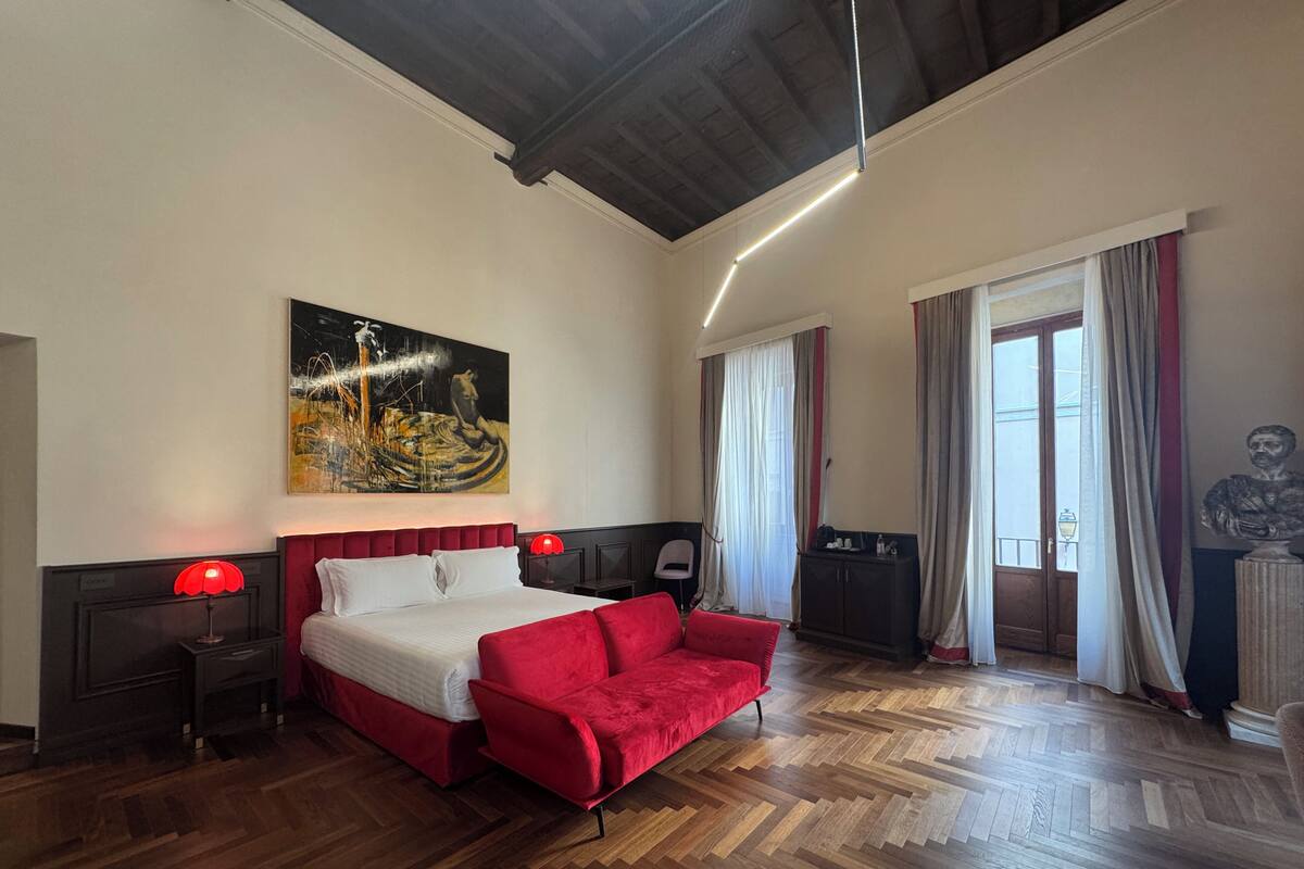 Ein Hotelzimmer mit einem Bett, einem roten Sofa, einem Bild an der Wand, einem Schrank und einer Statue.