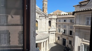 A view through a window of a courtyard with classical architecture, including a bell tower and a dome. - Palazzo Gambirasi Aparthotel Roma (Rome)
