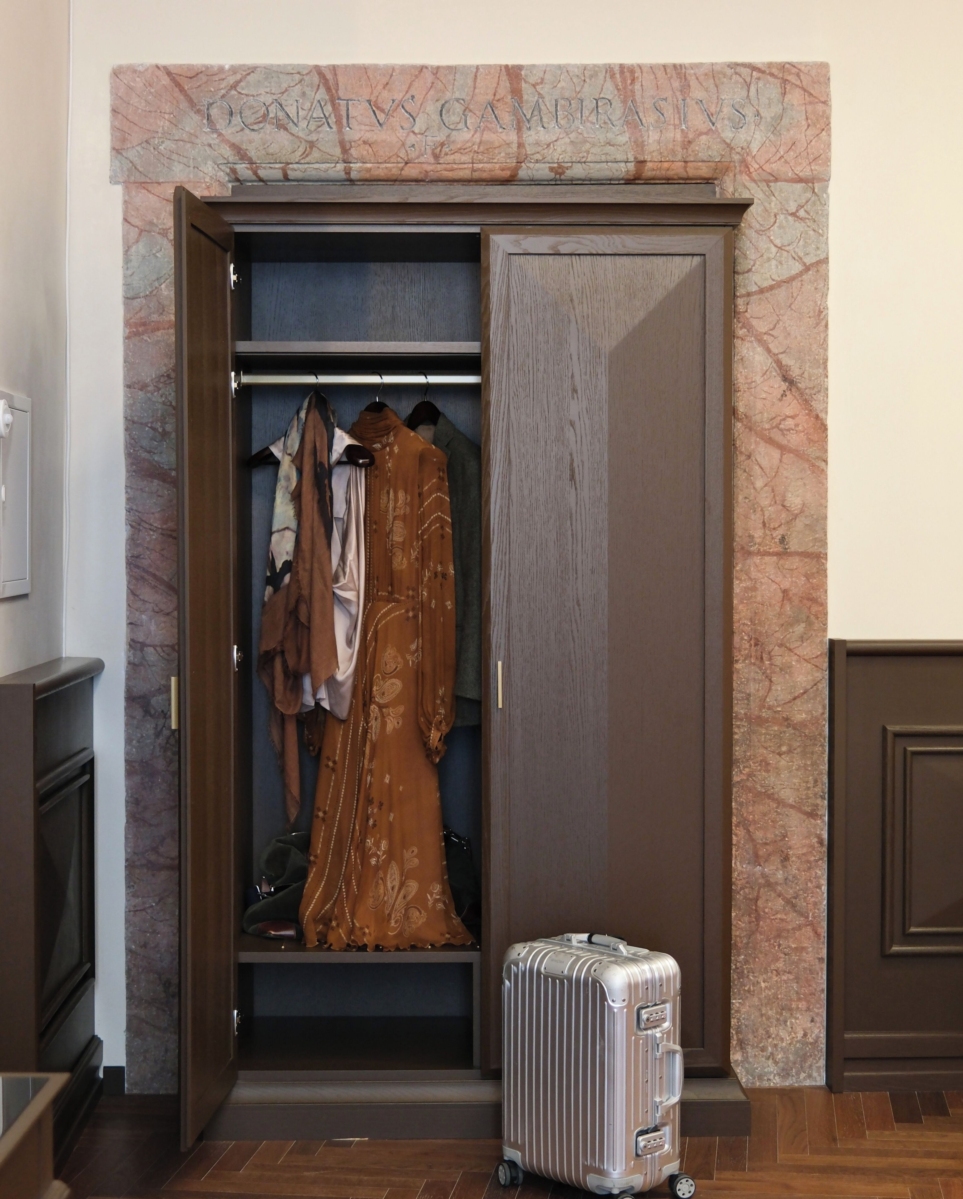 Ein Schrank mit Marmorwand, einem aufgehängten Kleidungsstück und einem Koffer.