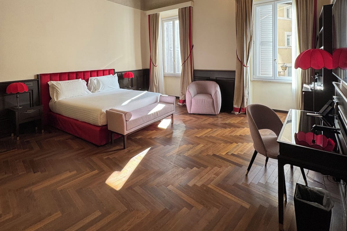 Ein Hotelzimmer mit einem Bett, einem Schreibtisch mit Klavier, einem Sessel und einem Fenster mit Vorhängen.