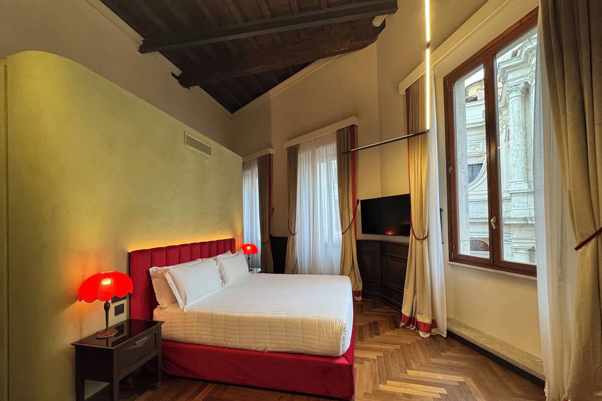 Ein Hotelzimmer mit Bett, Fernseher, Holzboden und einem Fenster mit Vorhängen.