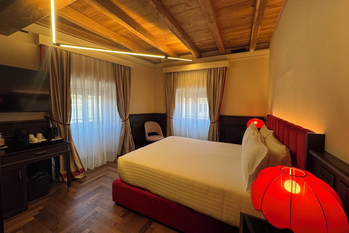 Ein Hotelzimmer mit Holzboden, einem Bett mit rotem Kopfteil, einem Schreibtisch mit Fernseher und einer roten Lampe.